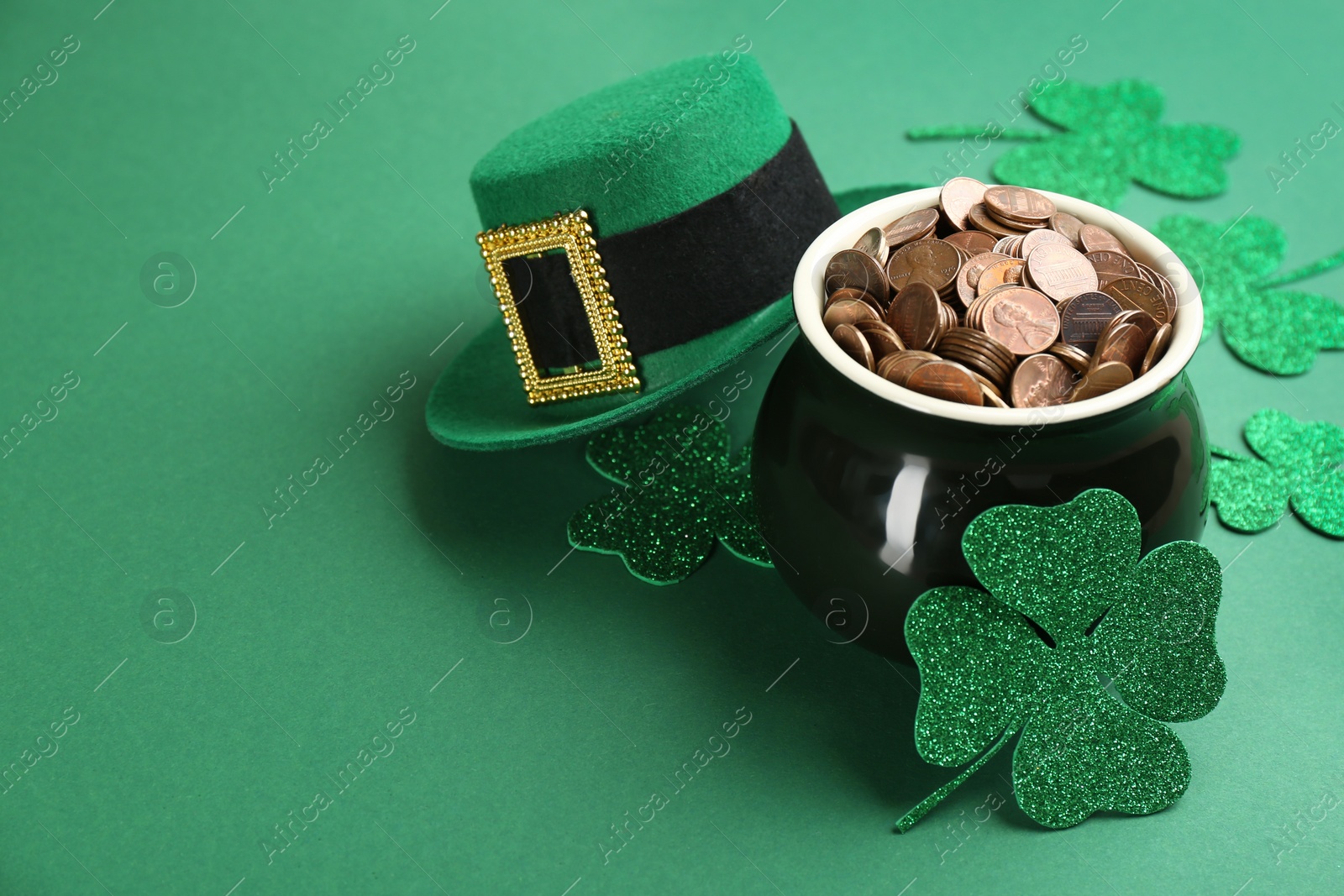 Photo of Pot of gold coins, hat and clover leaves on green background, space for text. St. Patrick's Day celebration