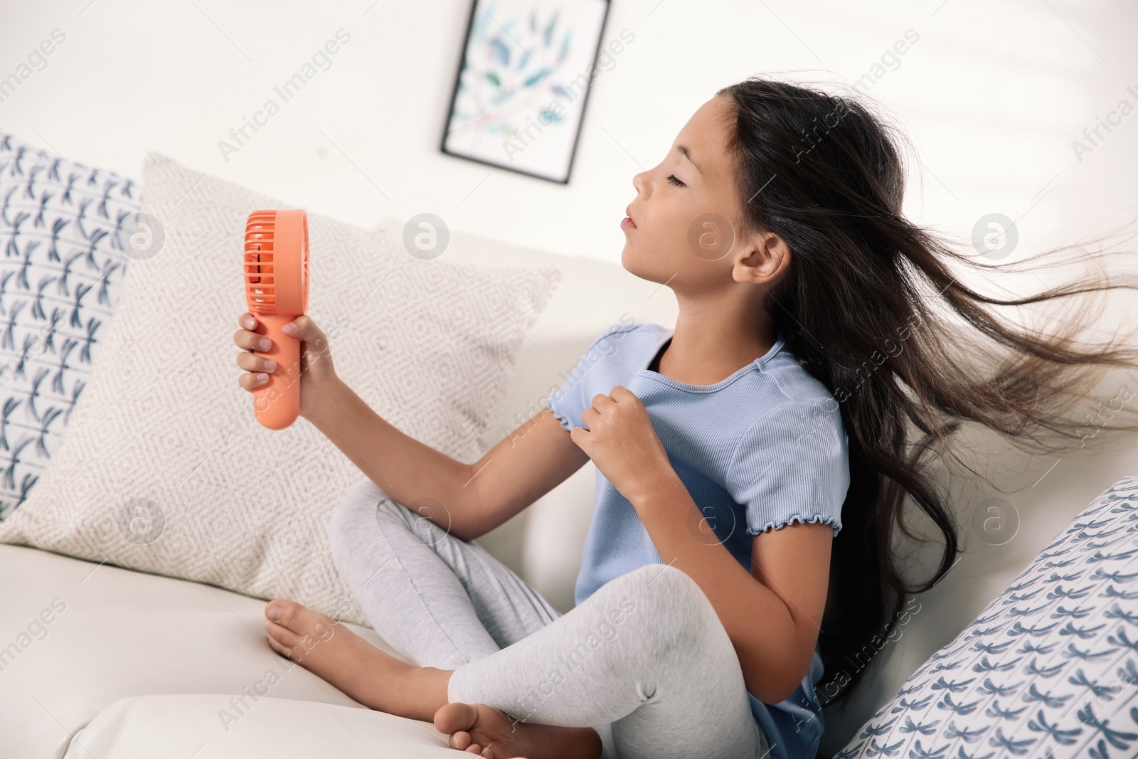 Photo of Little girl enjoying air flow from portable fan at home. Summer heat