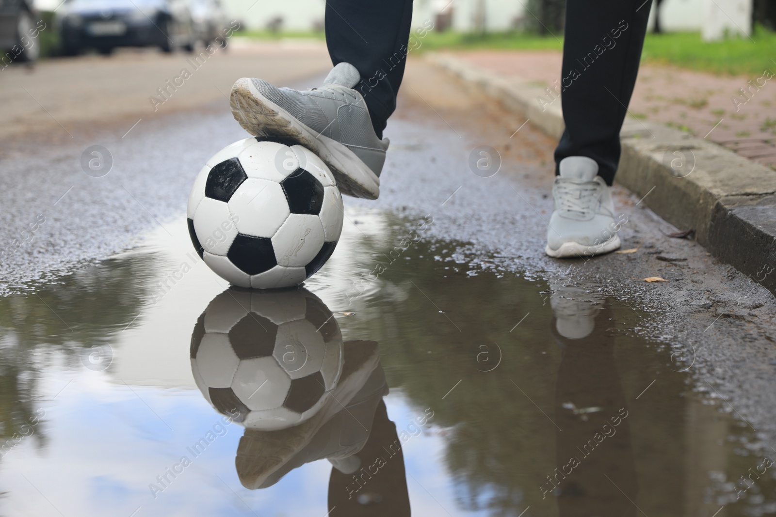 Photo of Man with soccer ball near puddle outdoors, closeup