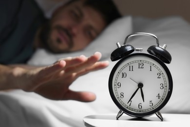 Sleepy man turning off alarm clock on nightstand in morning, closeup