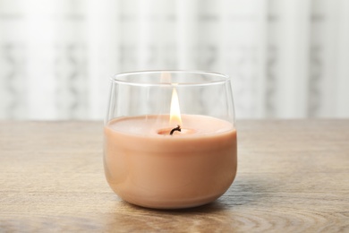 Photo of Burning candle in glass holder on wooden table