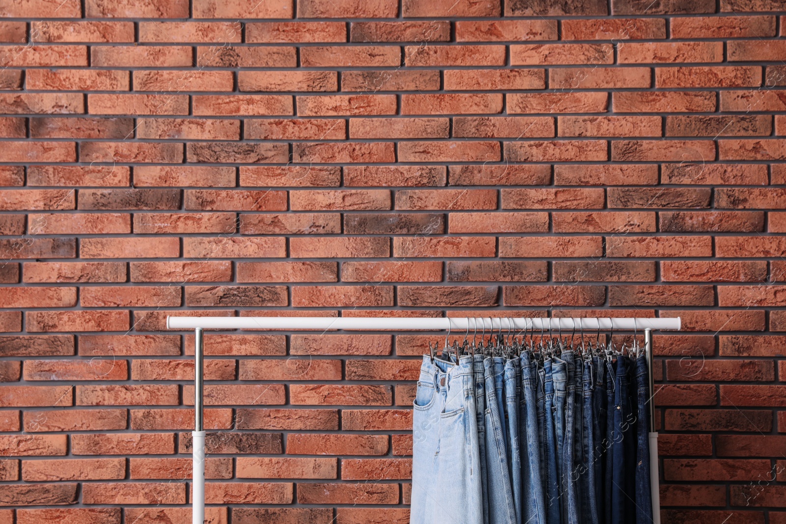 Photo of Rack with stylish jeans near brick wall. Space for text