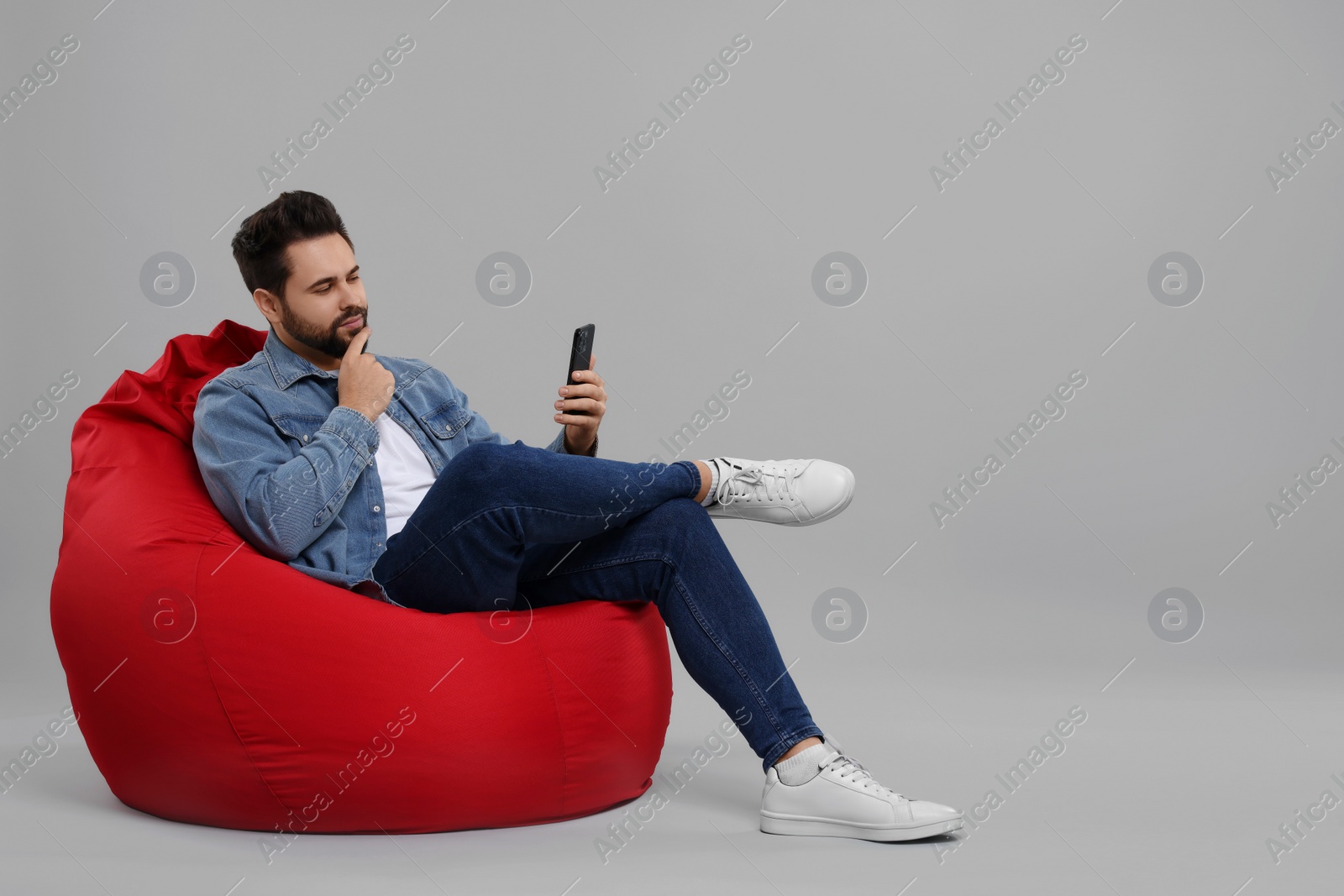 Photo of Handsome young man using smartphone on bean bag chair against grey background, space for text