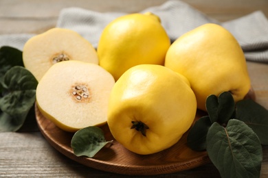 Fresh ripe organic quinces with leaves on wooden table, closeup