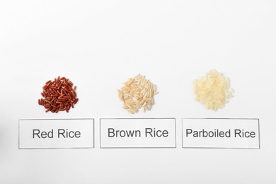 Photo of Different types of uncooked rice and cards on white background, top view