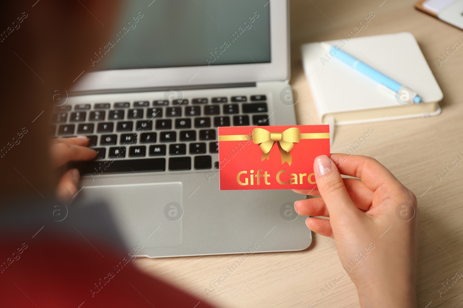 Photo of Woman with gift card and laptop at wooden table, closeup