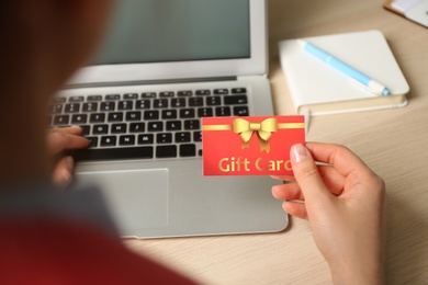 Woman with gift card and laptop at wooden table, closeup