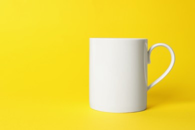 Photo of One white ceramic mug on yellow background. Space for text