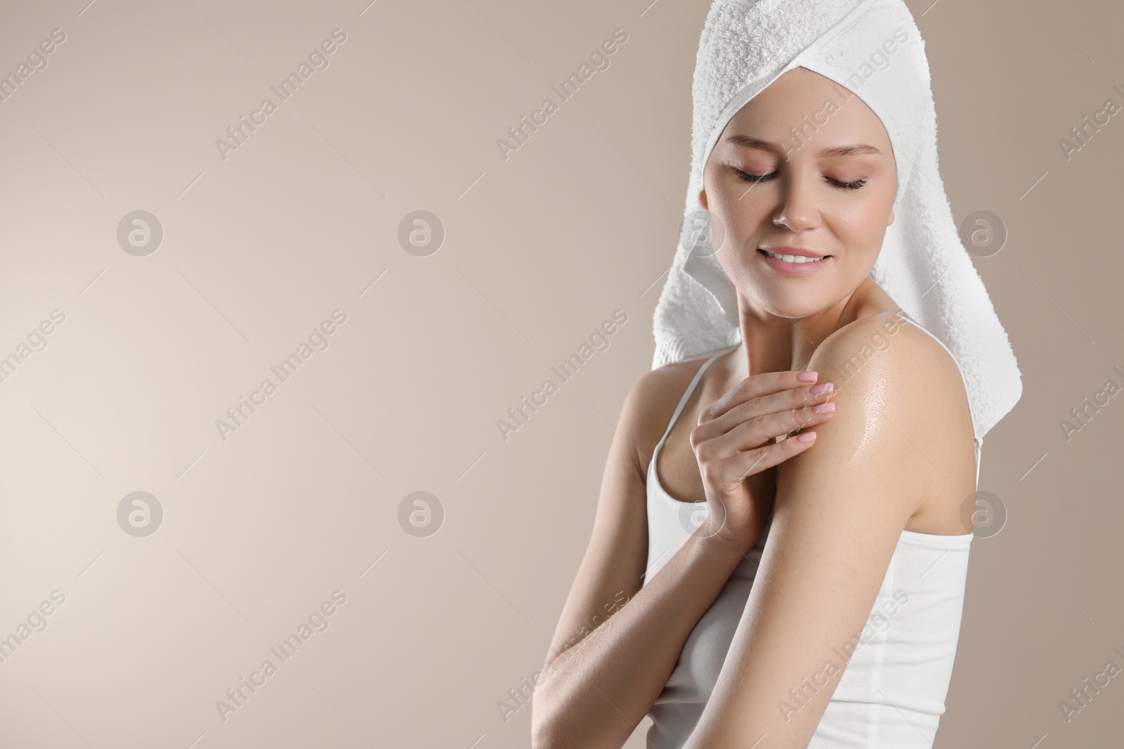 Photo of Happy woman applying body oil onto shoulder on beige background, space for text