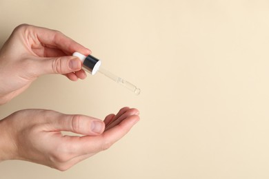 Photo of Woman applying cosmetic serum onto fingers on beige background, closeup. Space for text