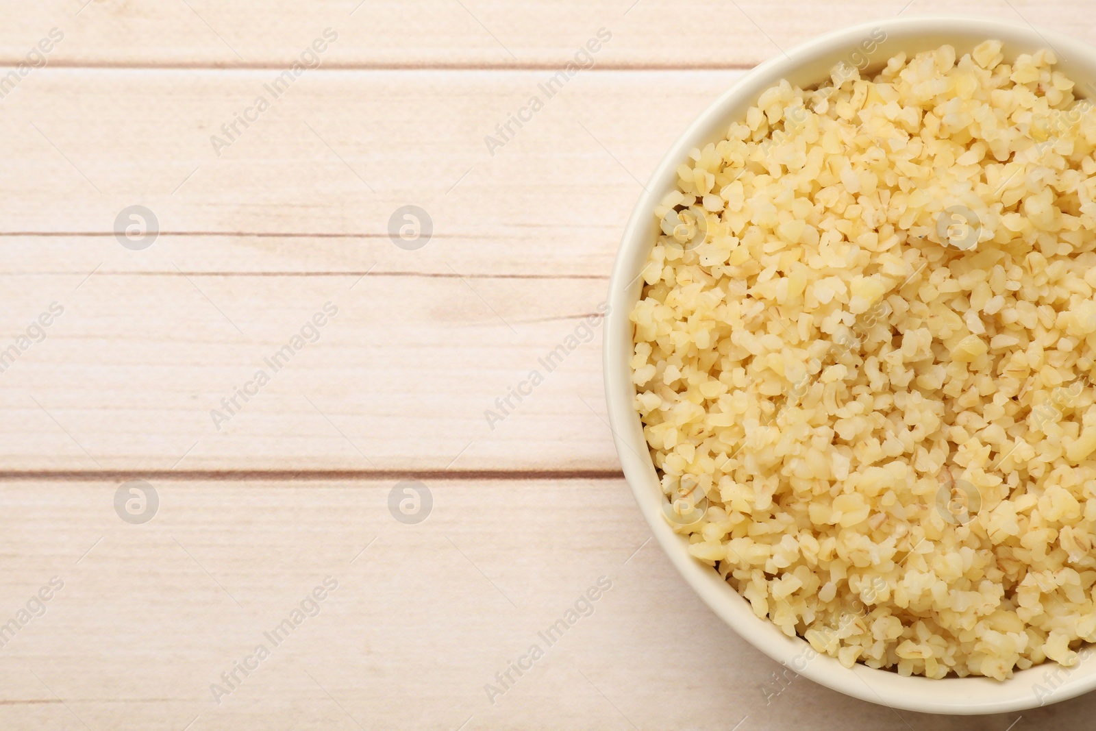 Photo of Delicious bulgur in bowl on wooden table, top view. Space for text