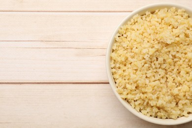 Photo of Delicious bulgur in bowl on wooden table, top view. Space for text