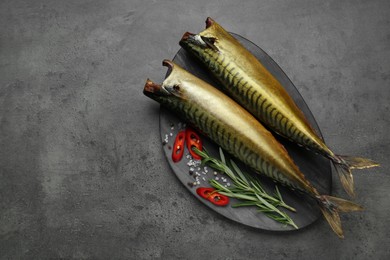 Delicious smoked mackerels and spices on dark grey table, flat lay. Space for text