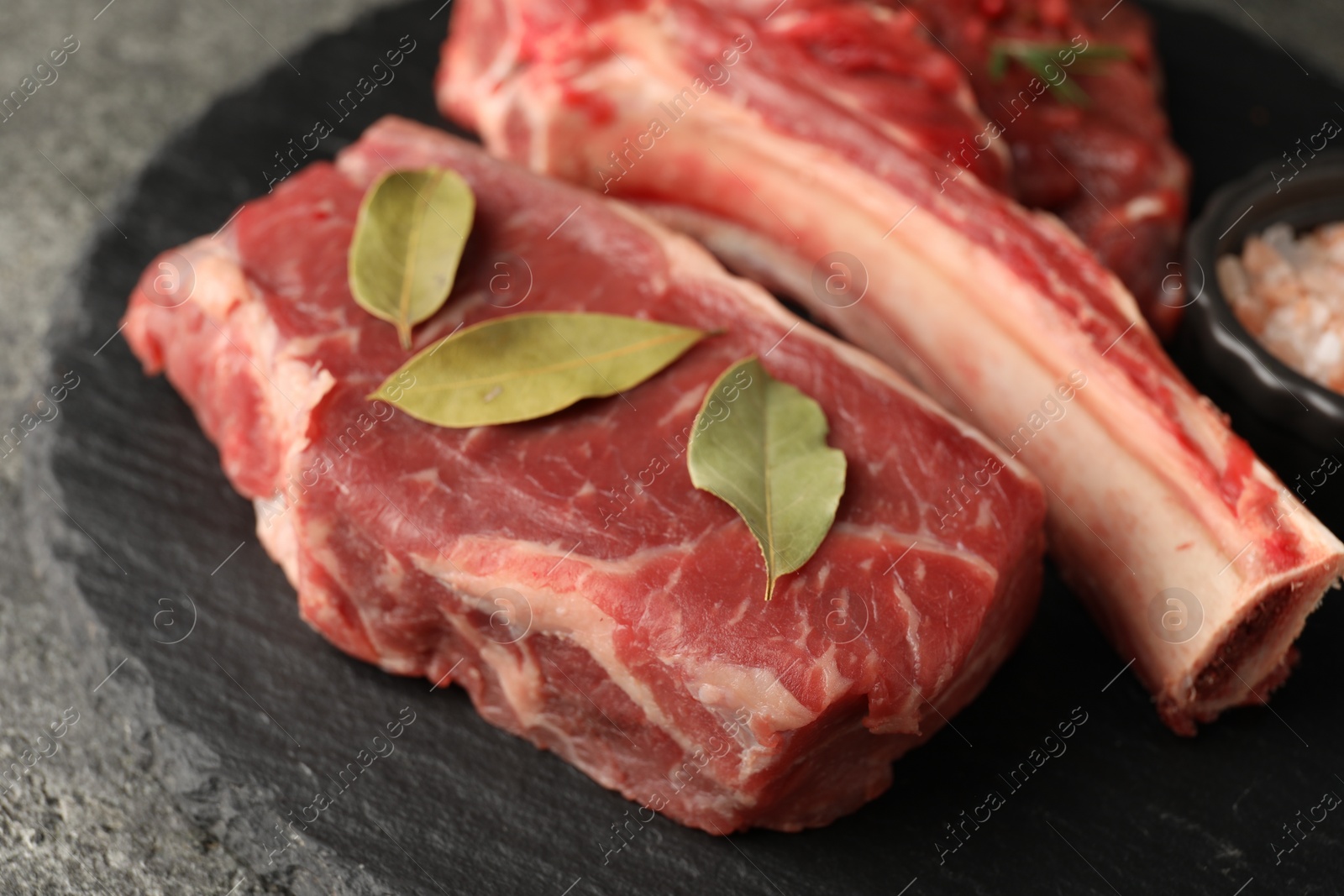 Photo of Pieces of raw beef meat and bay leaves on grey table, closeup