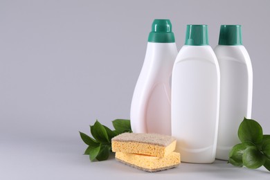 Bottles of cleaning product, sponges and green leaves on light background. Space for text