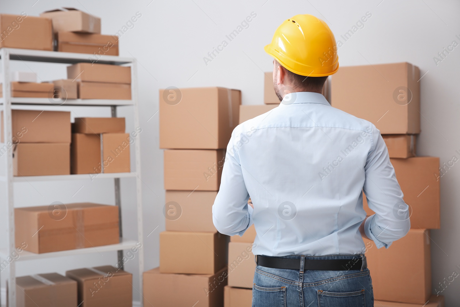 Photo of Young man near cardboard boxes at warehouse, back view