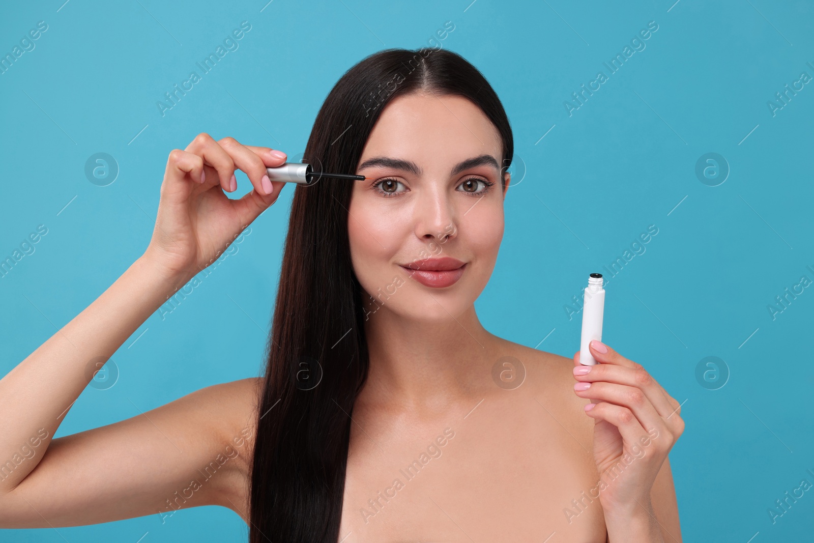 Photo of Beautiful woman applying serum onto her eyelashes on light blue background. Cosmetic product