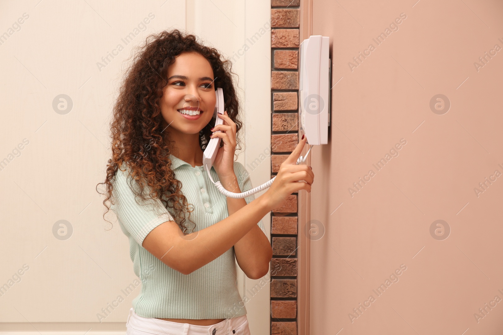 Photo of Young African-American woman answering intercom call indoors