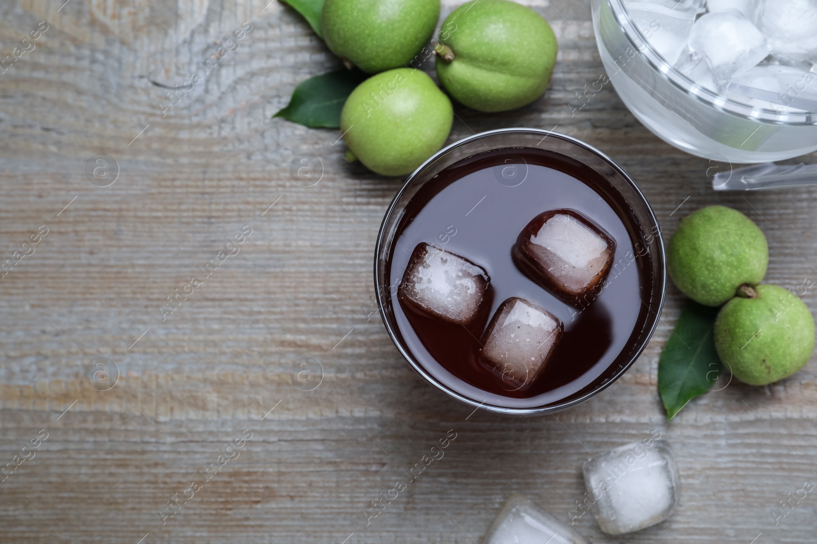 Photo of Delicious liqueur with ice and green walnuts on wooden table, flat lay. Space for text