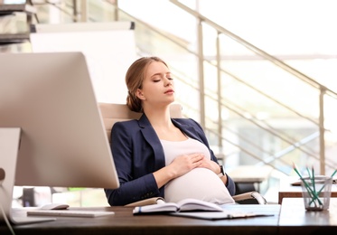 Photo of Young pregnant woman suffering from pain while working in office