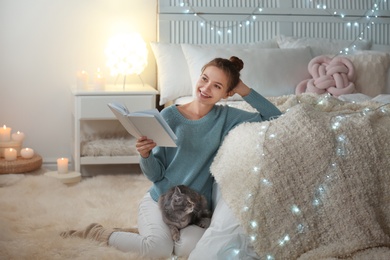 Young woman with cute cat reading book at home. Cozy winter