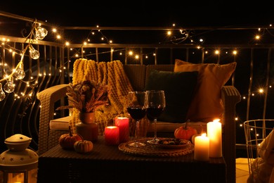 Photo of Glasses of wine, burning candles and autumn decor on outdoor terrace in evening