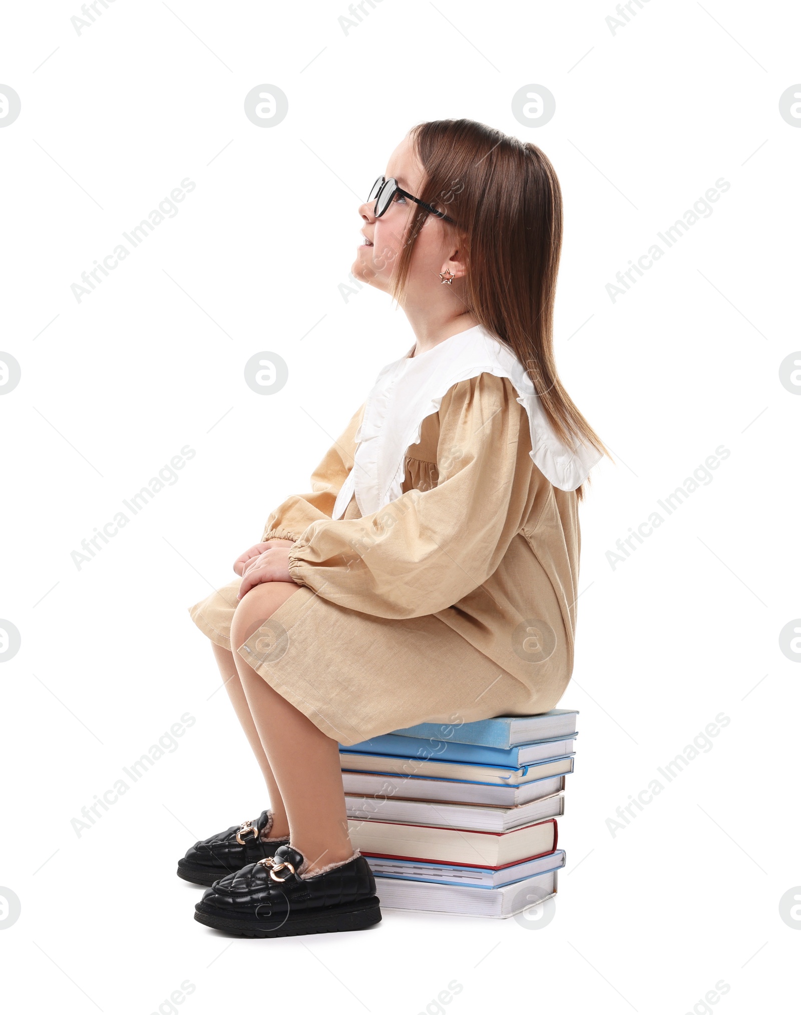 Photo of Cute little girl in glasses sitting on stack of books against white background