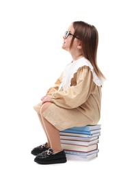 Cute little girl in glasses sitting on stack of books against white background