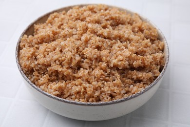 Photo of Tasty wheat porridge in bowl on white tiled table, closeup