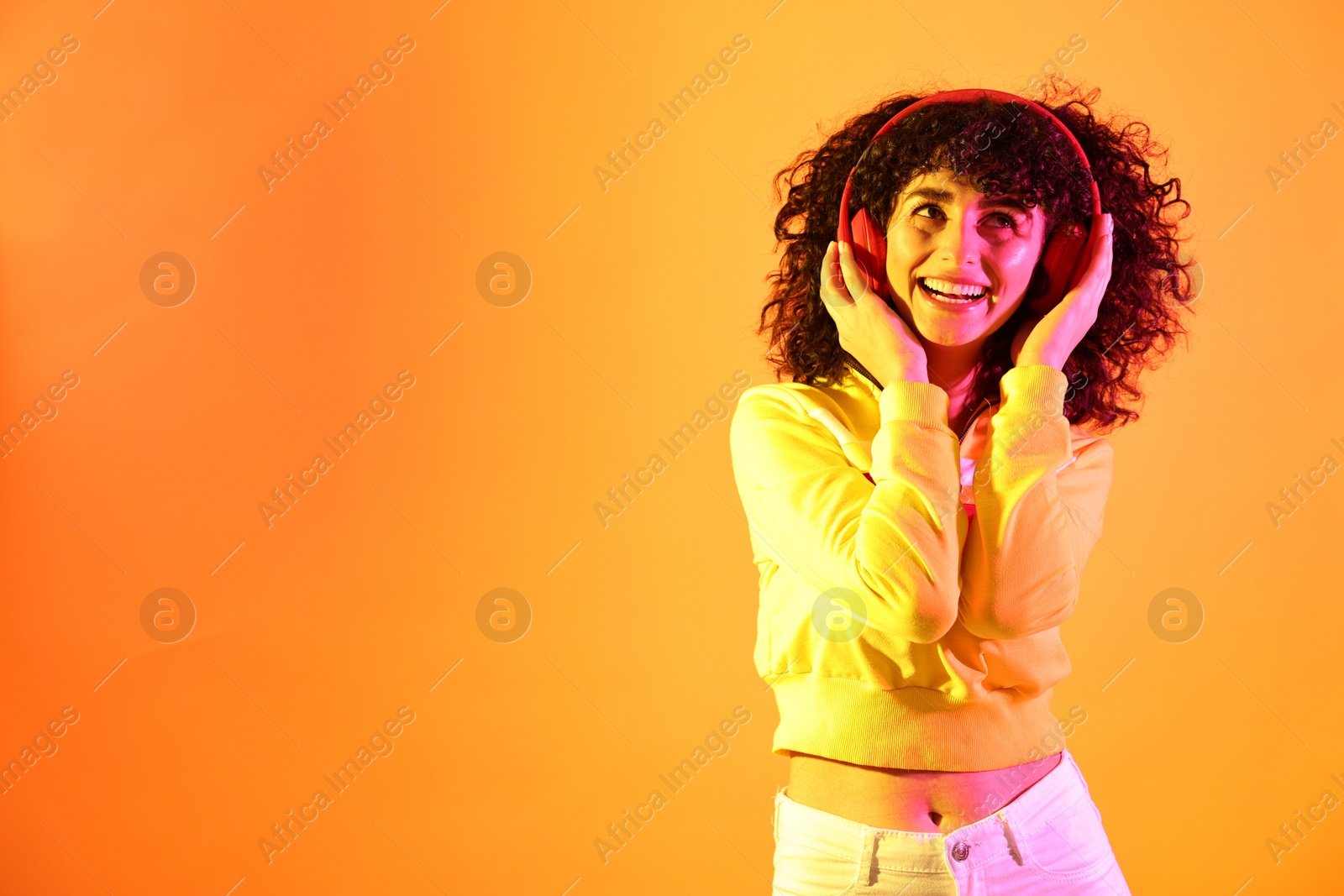 Photo of Beautiful young woman listening to music with headphones on color background in neon lights. Space for text