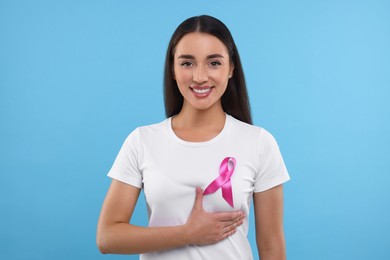 Photo of Beautiful happy woman with pink ribbon on light blue background. Breast cancer awareness