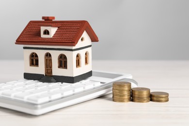 Photo of Mortgage concept. Model house, stacks of coins and calculator on white wooden table against light grey background