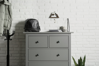 Photo of Grey chest of drawers near white brick wall indoors