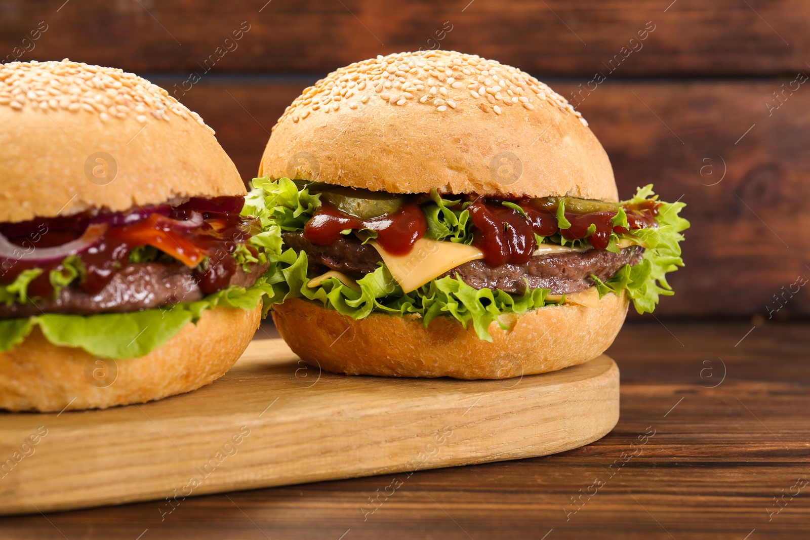 Photo of Board with delicious cheeseburgers on wooden table, closeup