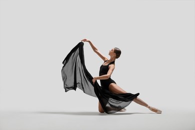 Photo of Graceful young ballerina practicing dance moves with black veil on white background