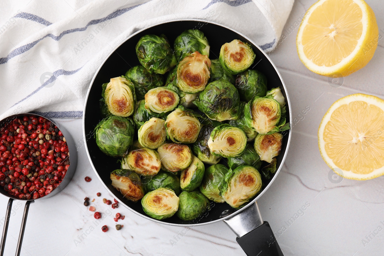 Photo of Delicious roasted Brussels sprouts in frying pan, peppercorns and lemon on white textured table, flat lay