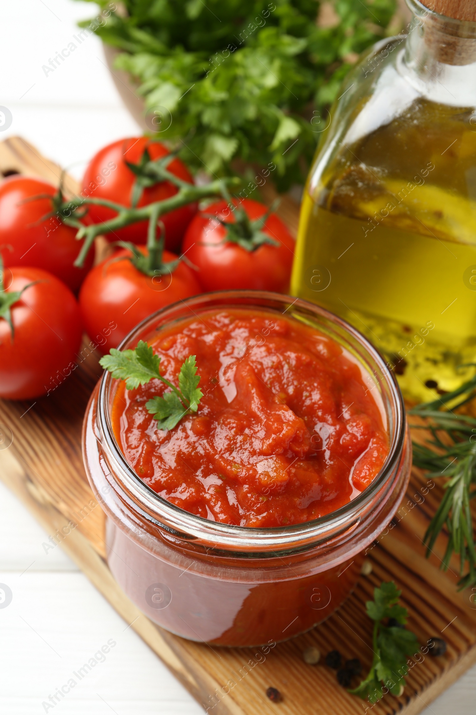 Photo of Homemade tomato sauce in jar and fresh ingredients on white table, closeup