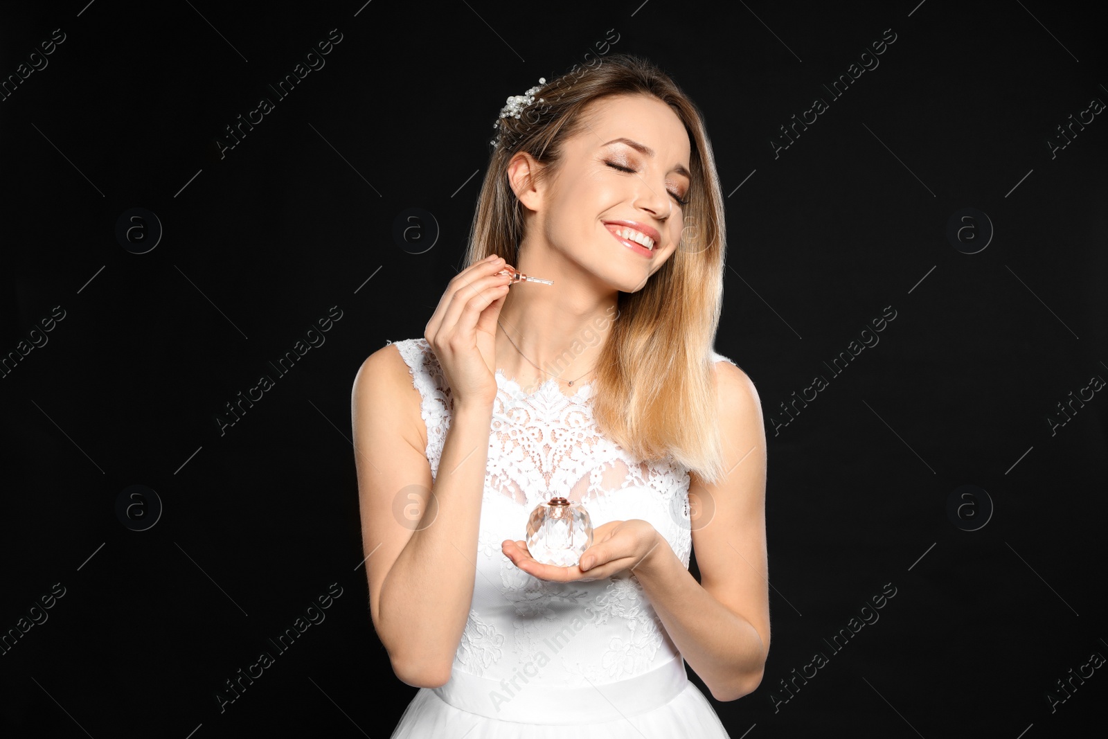 Photo of Beautiful young bride applying perfume against black background