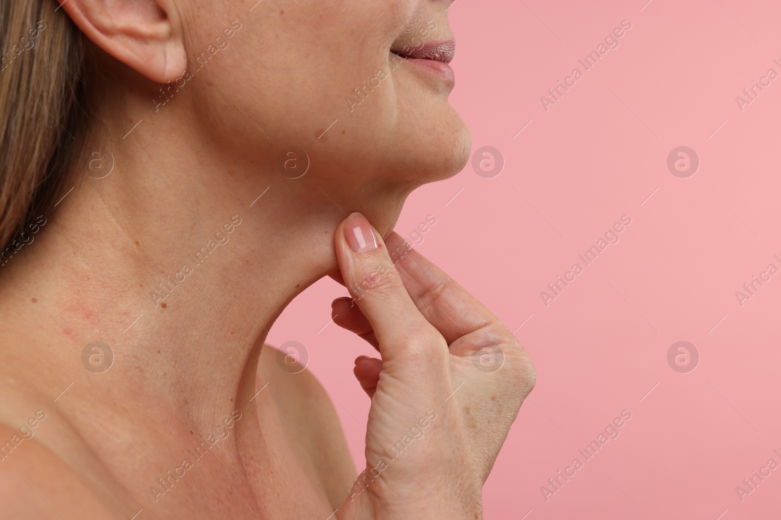 Photo of Mature woman touching her neck on pink background, closeup. Space for text