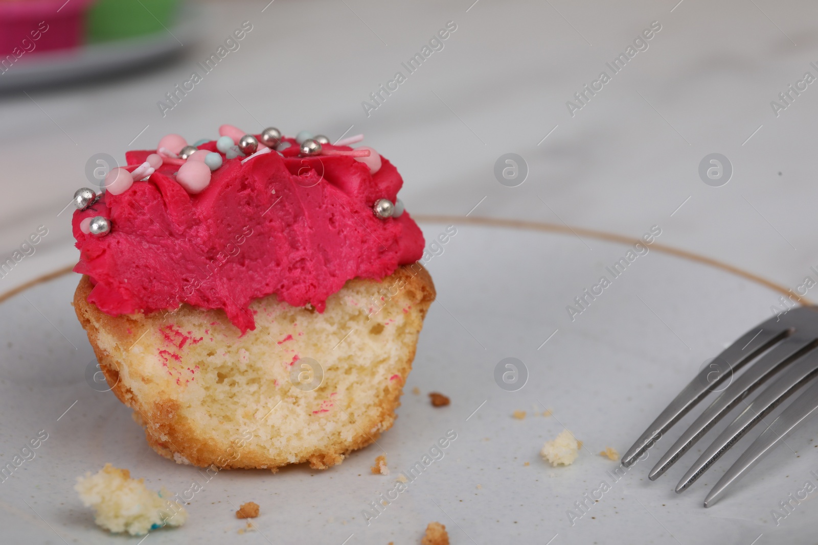 Photo of Bitten cupcake with cream on plate, closeup