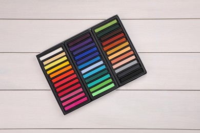 Photo of Set of colorful pastels in box on white wooden table, top view. Drawing materials