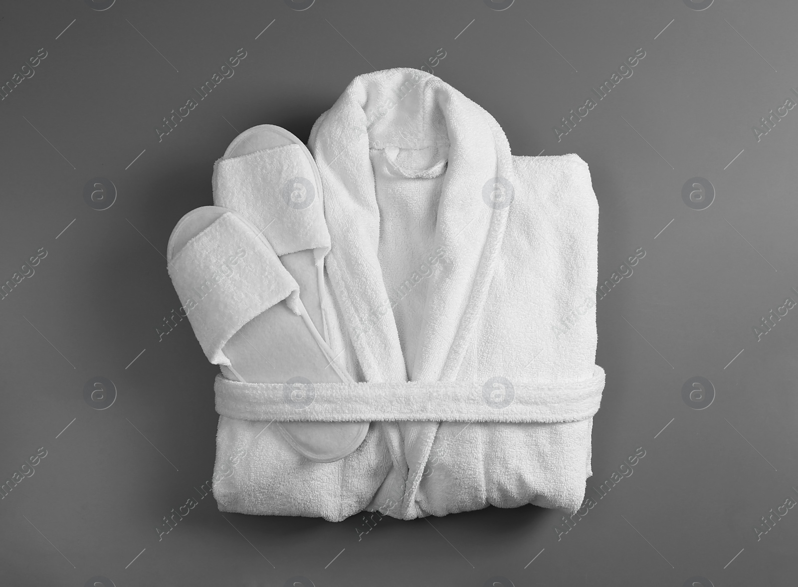 Photo of Clean folded bathrobe and slippers on grey background, top view