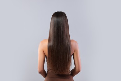 Photo of Hair styling. Woman with straight long hair on grey background, back view