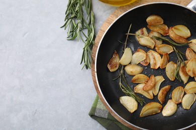 Frying pan with fried garlic cloves and rosemary on gray table, top view. Space for text