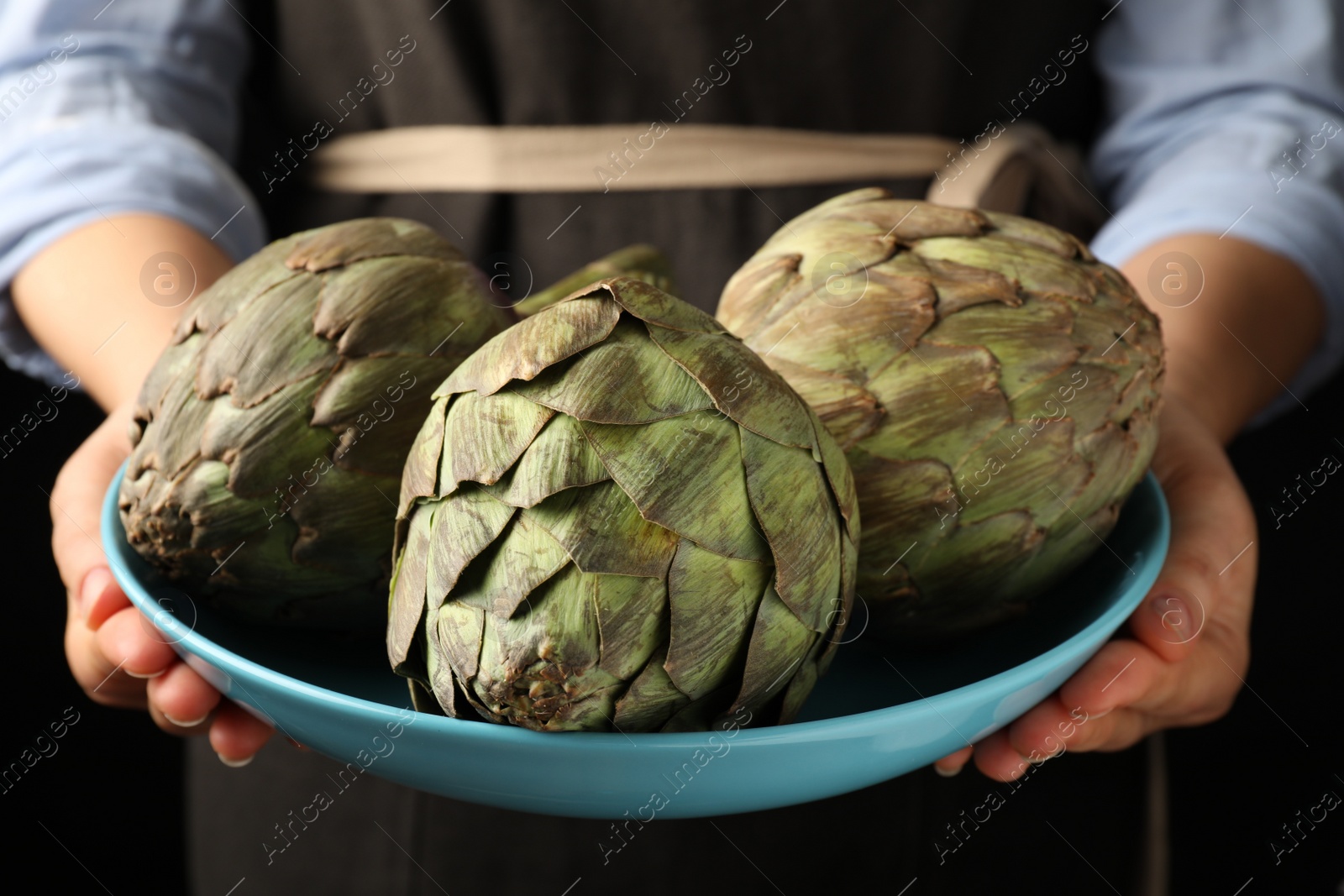 Photo of Woman holding bowl with fresh raw artichokes, closeup