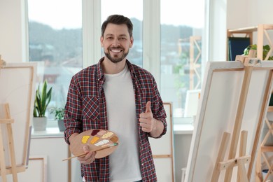 Photo of Handsome man with painting supplies showing thumb up in studio. Creative hobby