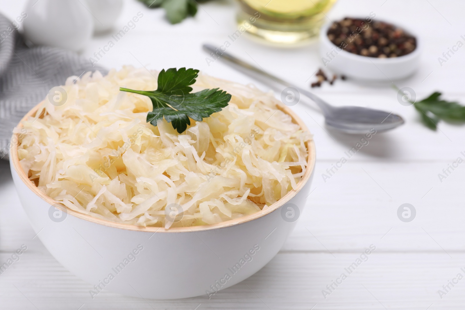 Photo of Bowl of tasty sauerkraut on white wooden table, closeup