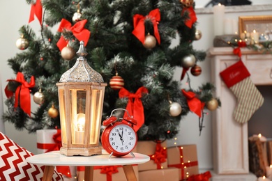 Photo of Lantern and alarm clock on table near decorated Christmas tree in stylish living room interior