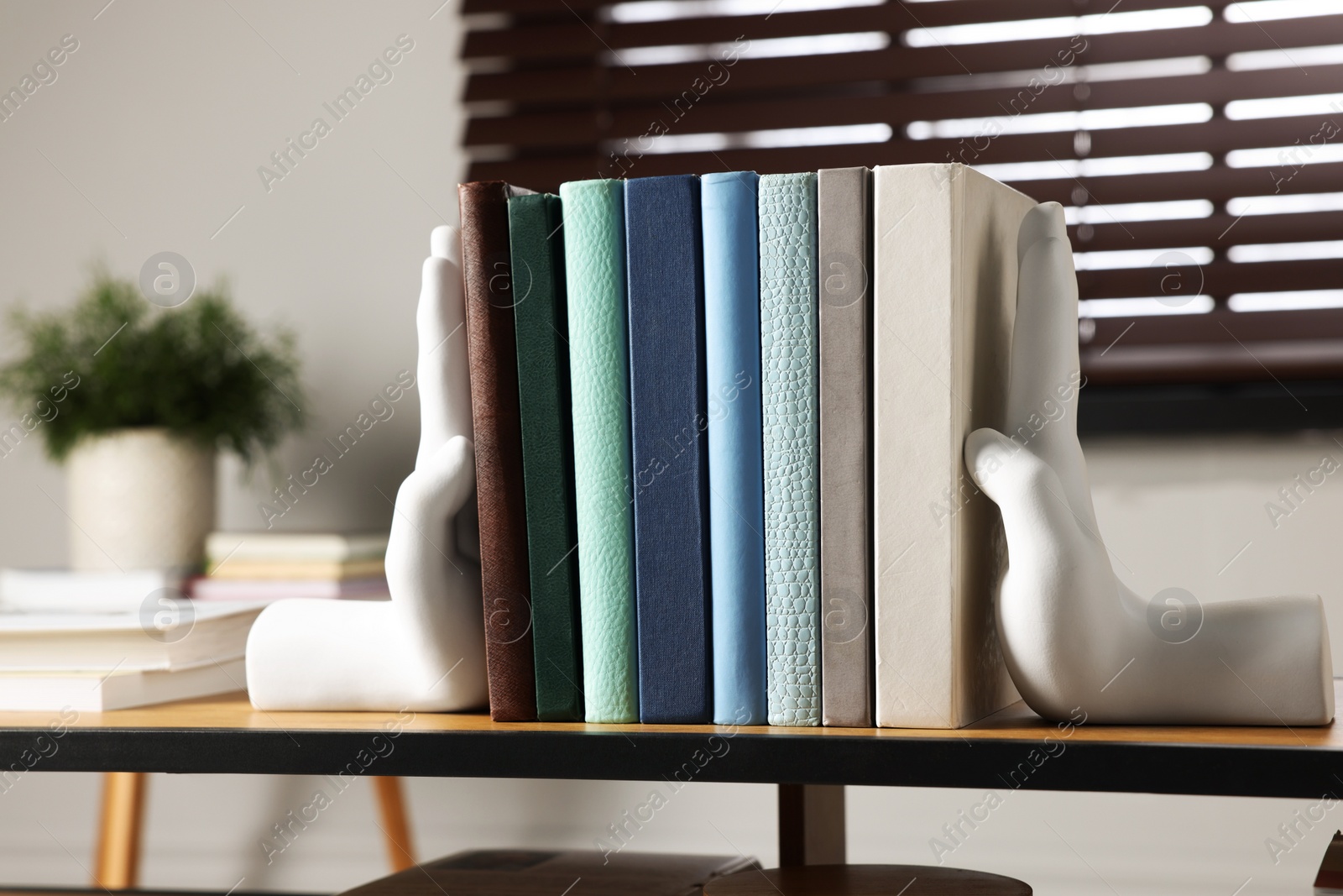 Photo of Beautiful hand shaped bookends with books on shelf indoors