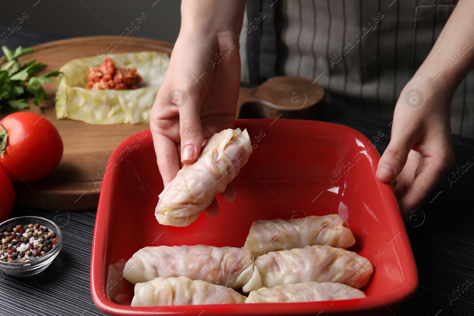 Photo of Woman putting uncooked stuffed cabbage roll into baking dish at black table, closeup